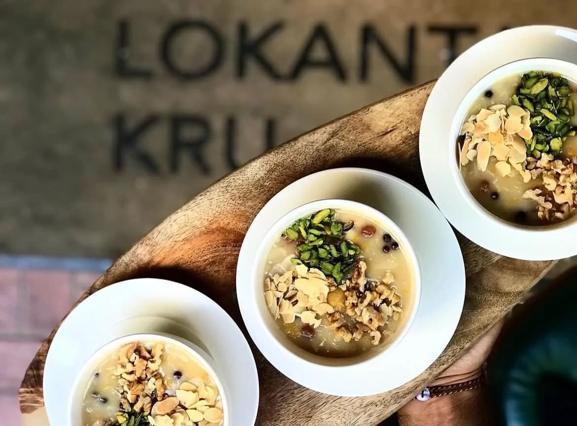 Three bowls of asure (Noah's pudding) shot from above; 'Lokanta Kru' engraved into the concrete wall behind.
