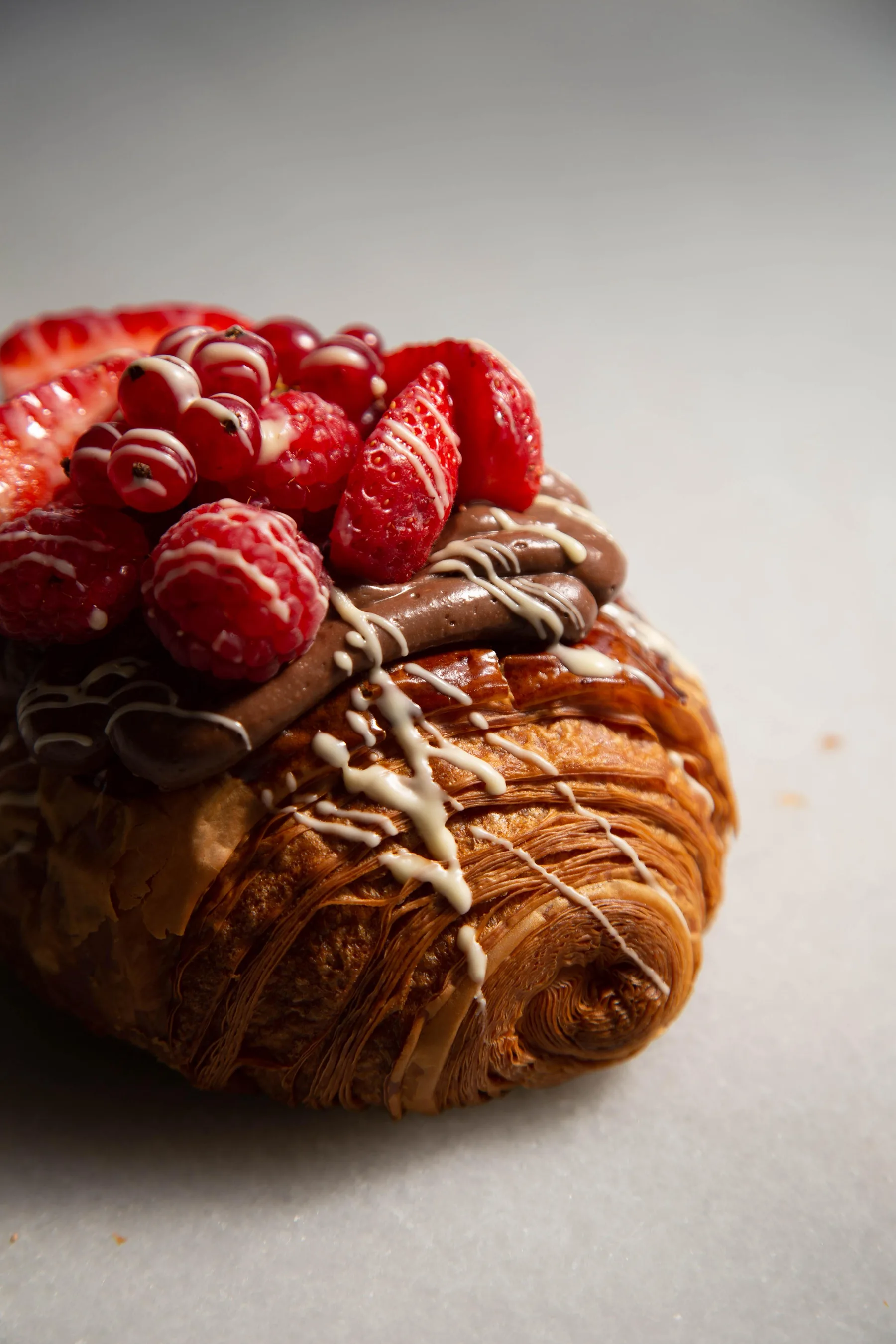 Close-up of a croissant with visible layers, topped with chocolate cream, strawberries and raspberries.