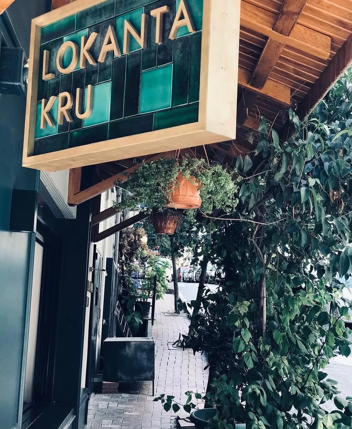 Lokanta Kru's green-tiled exterior sign with gold lettering; a wooden awning, ivy and terracotta pots.