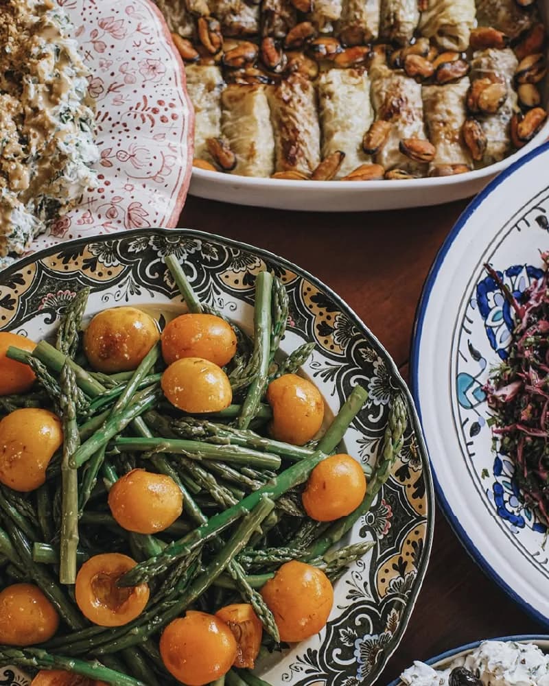 Patterned plates of meze and olive-oil dishes arranged side by side on a crowded lunch table.