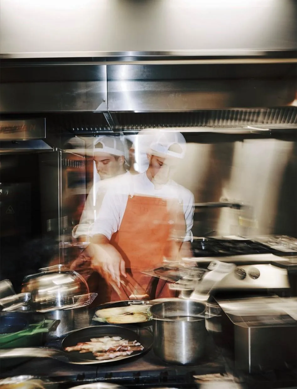 Two cooks preparing service in a steel kitchen; motion blurred by a long exposure.